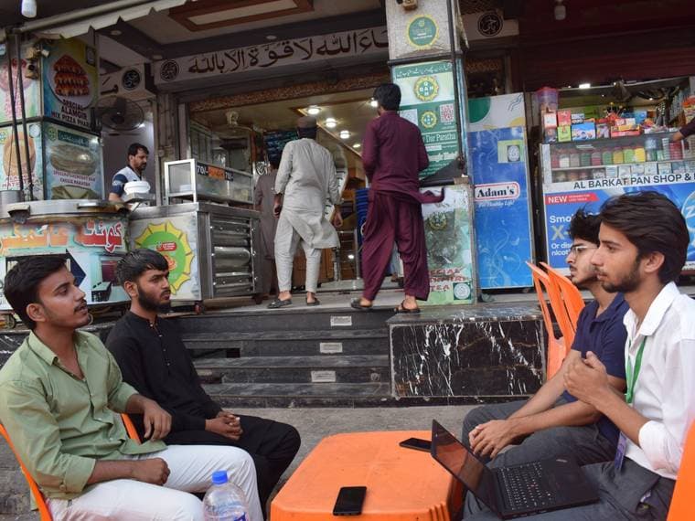 Two attendees with a laptop at a roadside table outside Queeta Hotel, the very first AI Baithak