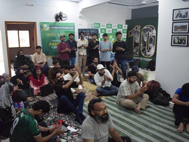 A full room seated on the floor at Session 3, partner banners along the wall