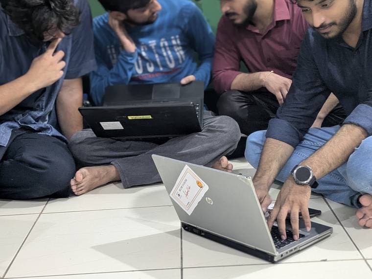 Attendees leaning in around a single laptop on the floor at Session 3
