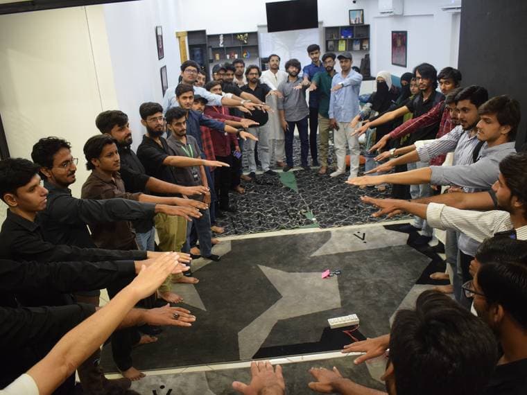 A wide circle of attendees reaching into the middle at Session 5