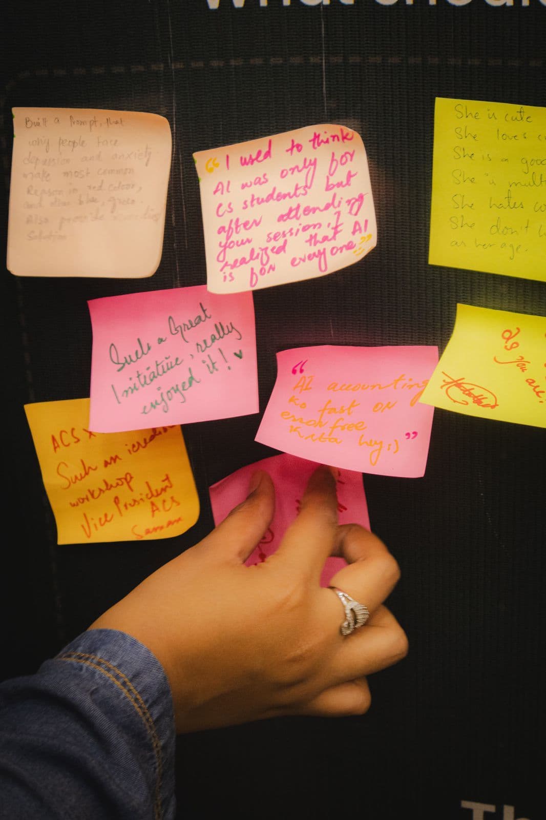 A hand adding a sticky note to a wall of handwritten notes left by attendees; one reads: I used to think AI was only for CS students, but after attending your session I realised that AI is for everyone