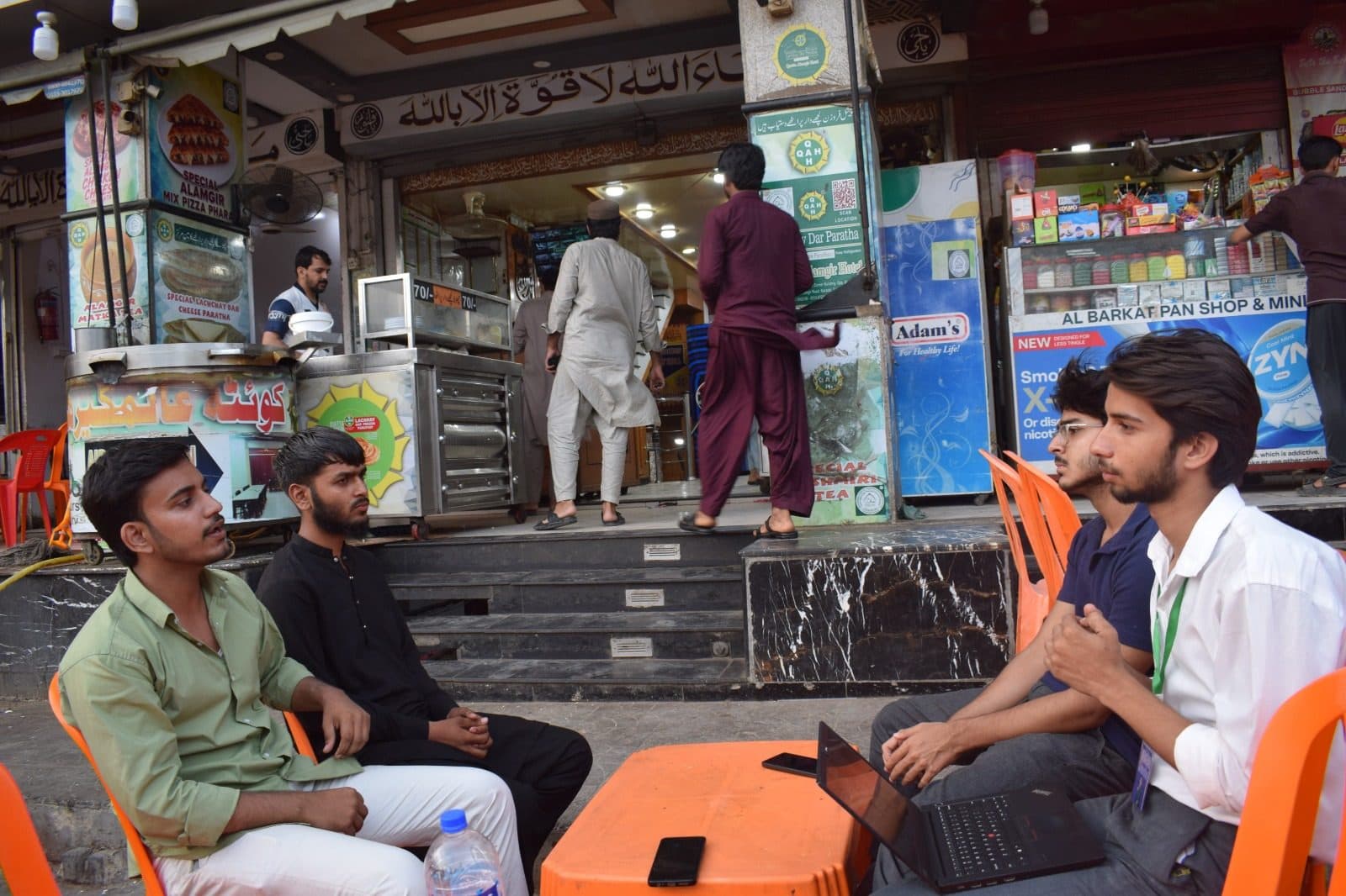 Two attendees with a laptop at a roadside table outside Queeta Hotel, the very first AI Baithak