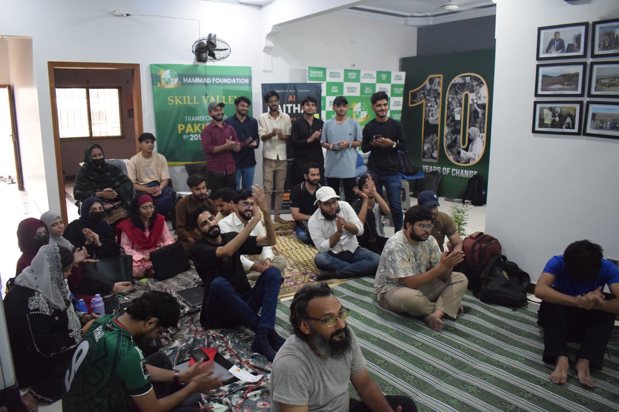 A full room seated on the floor at Session 3, partner banners along the wall
