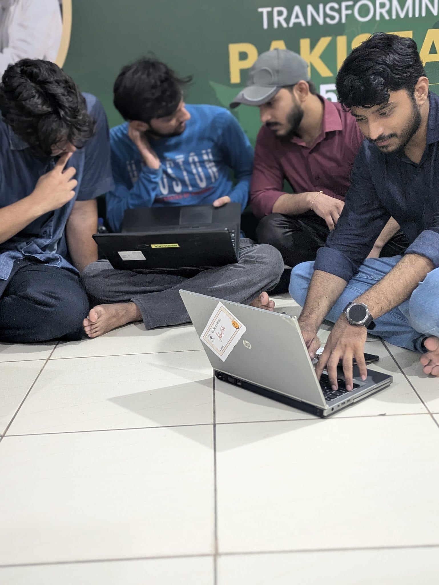 Attendees leaning in around a single laptop on the floor at Session 3